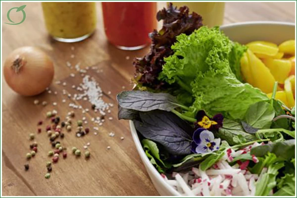 Das Bild zeigt einen Salat in einer Schüssel, mit verschiedenen Gewürzen, einer Zwiebel und unterschiedlichen Dips daneben