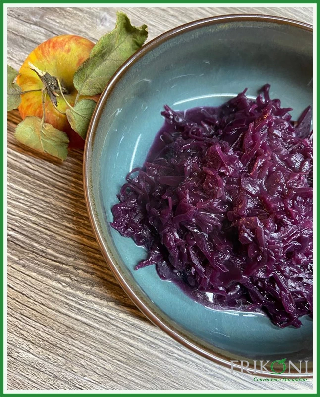 Bild zeigt den zubereiteten Apfel-Rotkohl auf einem türkisfarbenem Teller. Daneben zur Dekoration ein Apfel mit Strunk und grünen Blättern,