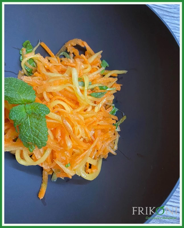 Das Bild zeit den Mango-Möhrensalat auf einem dunkelblauen Teller, garniert mit frischen Minzblättern.