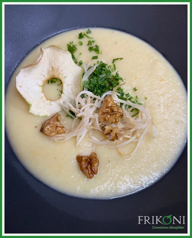 Bild zeigt die Suppe auf einem dunkelblauen Teller, garniert mit einer Apfelscheibe, Walnüssen und grüner Petersilie