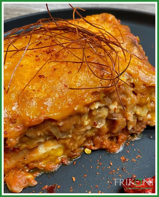 Bild zeitg die zubereitete Lasagne auf einem schwarzen Teller, dekoriert mit einer roten Chili