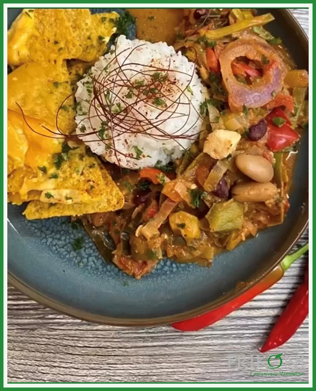 Bild zeigt die zubereitete Teas-Pfanne auf einem dunkelblauen Teller mit braunem Rand, daneben rote Paprika zur Dekoration.