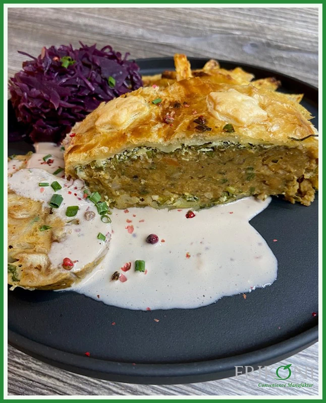 Bild zeigt ein halbes, aufgeschnittenes Stück des Bratens, angerichtet mit Rotkohl und einer weißen Sauce auf einem schwarzen Teller