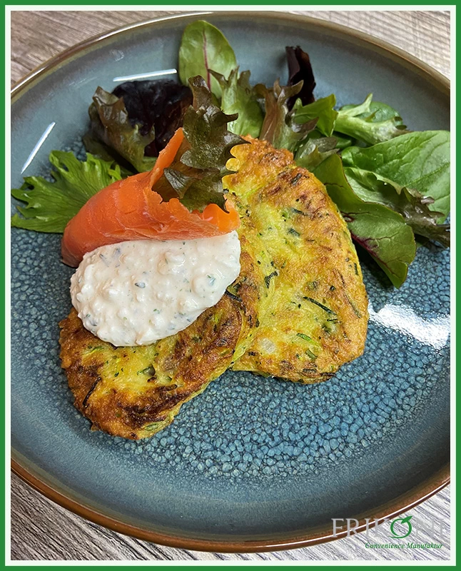 Bild zeigt die Zucchini-Puffer auf einem Wildkräuterbett, garniert mit Räucherlachs und einem weißen Dressing